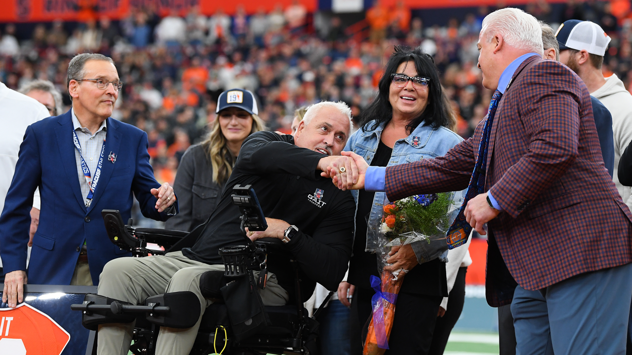 Seated in a motorized wheelchair, Paul Gait shakes Gary Gait's hand during his jersey retirement ceremony at Syracuse's JMA Wireless Dome.